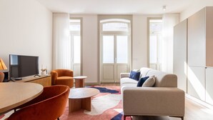 Un salon moderne avec un téléviseur, un fauteuil orange, un canapé beige et une table basse.