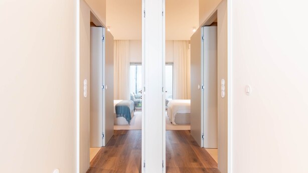 Un couloir menant à une chambre à coucher qui contient un lit, une chaise et une fenêtre.