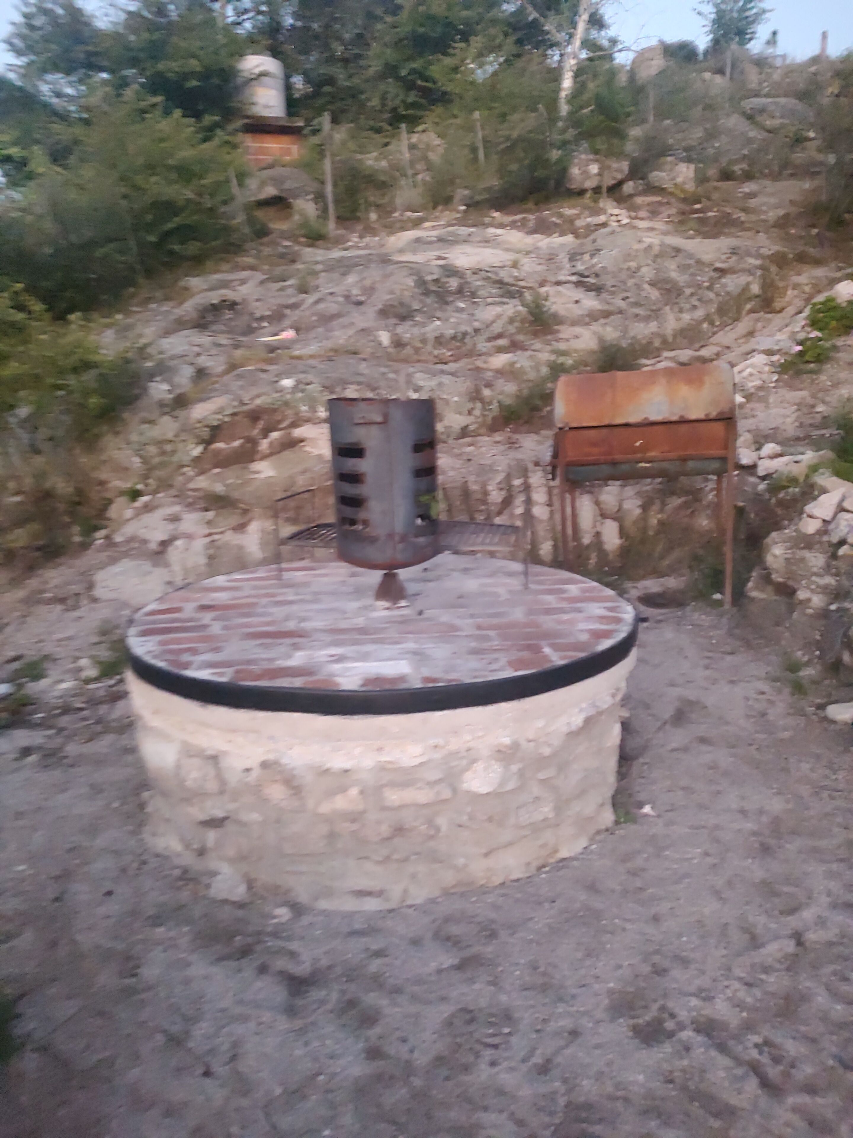 A circular stone structure with a metal speaker and a wooden chair.