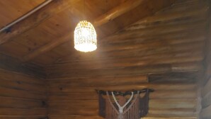 A wooden cabin bedroom with a bed, pillows, a hanging macrame, and a hanging light fixture.