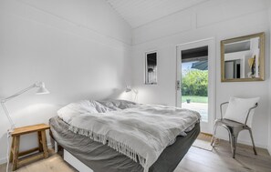 Ein Schlafzimmer mit Bett, Nachttischlampen, einem Sessel, einem Spiegel und einer Tür zu einem Außenbereich.