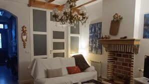 Un salon avec un canapé blanc, une table basse en bois, un lustre, une cheminée et une porte donnant sur une autre pièce.