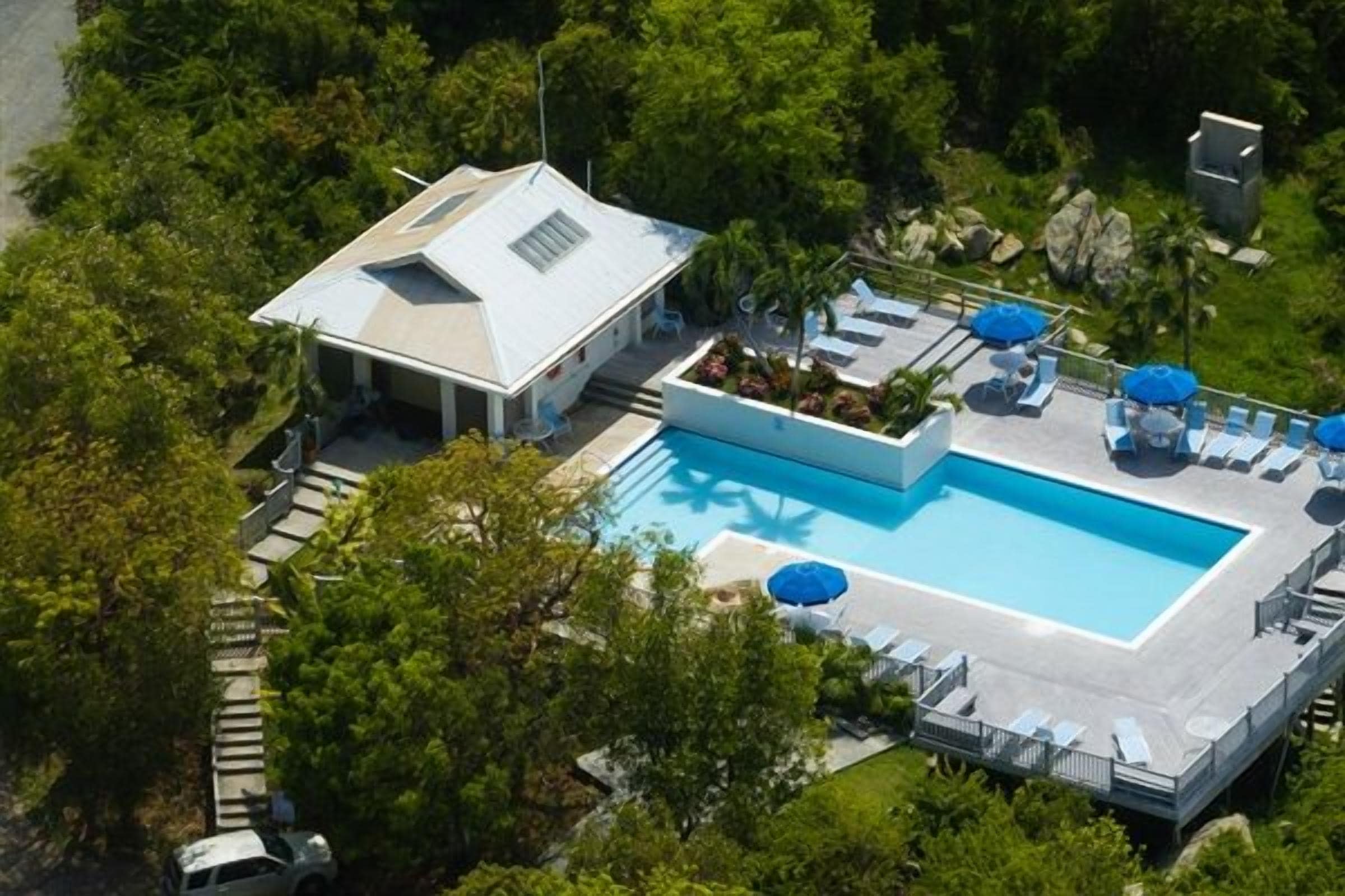 An aerial view of a property with a swimming pool, lounge chairs, and umbrellas.