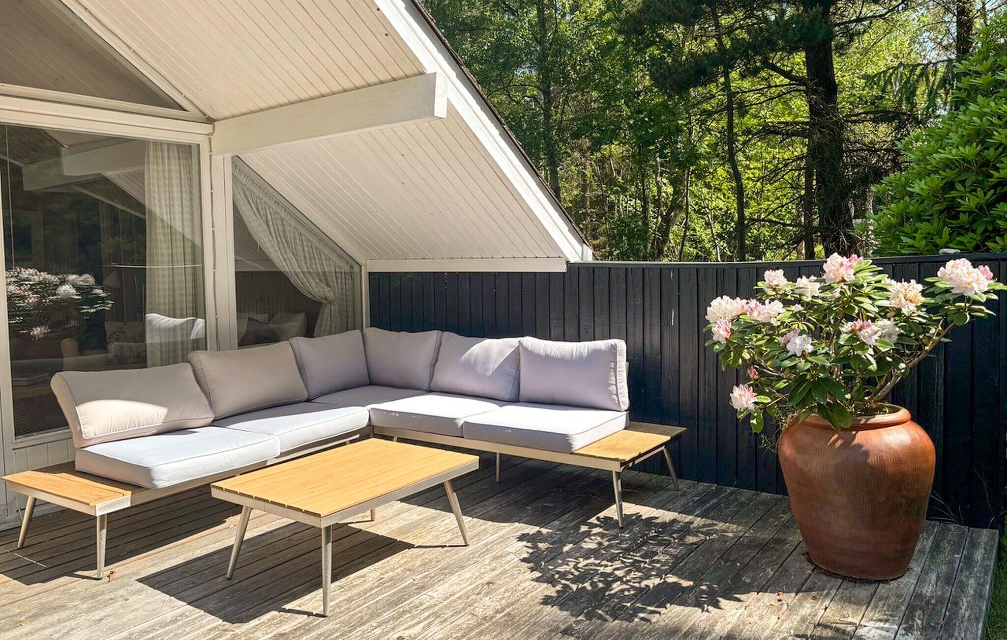 Un espacio exterior moderno con un sofá modular, una mesa de centro de madera y una planta grande en maceta.