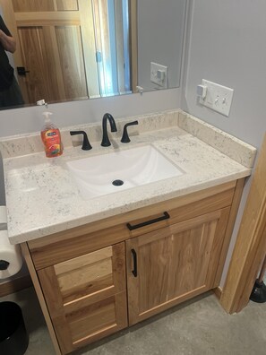 A bathroom with a white sink, black faucets, a wooden vanity, and a mirror above the sink.