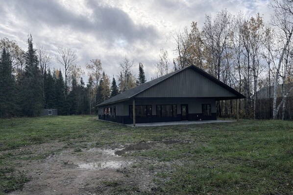 A single-story building with a large open porch, surrounded by a grassy field and trees.