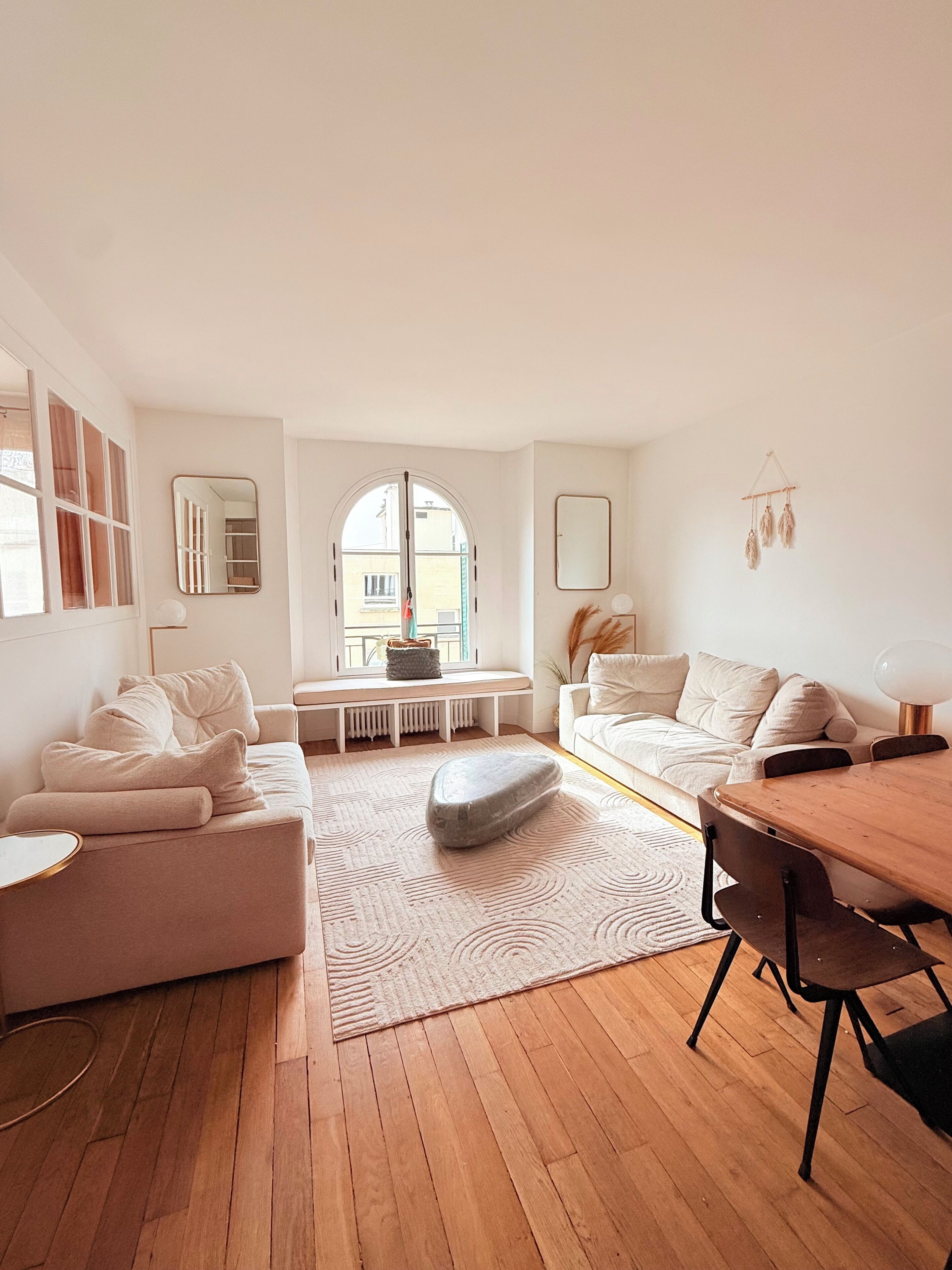 A modern living room with a sofa, a dining table, a stone accent, and a view through a large window.