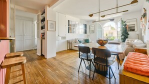 A spacious living area with a wooden floor, a dining table with chairs, a sofa, and a large window providing natural light. - Boho-chic cocoon in Neuilly-sur-Seine. (Neuilly-sur-Seine)