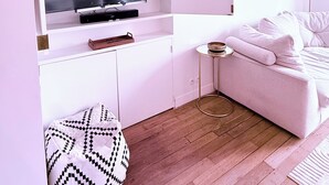 A modern living room with a flat-screen TV, white furniture, a small round table, and a patterned ottoman. - Boho-chic cocoon in Neuilly-sur-Seine. (Neuilly-sur-Seine)