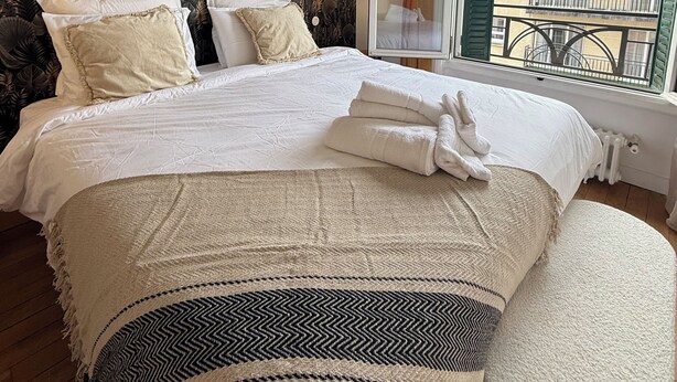 A bedroom with a large bed, a window with a view of buildings, and a patterned wallpaper. - Boho-chic cocoon in Neuilly-sur-Seine. (Neuilly-sur-Seine)