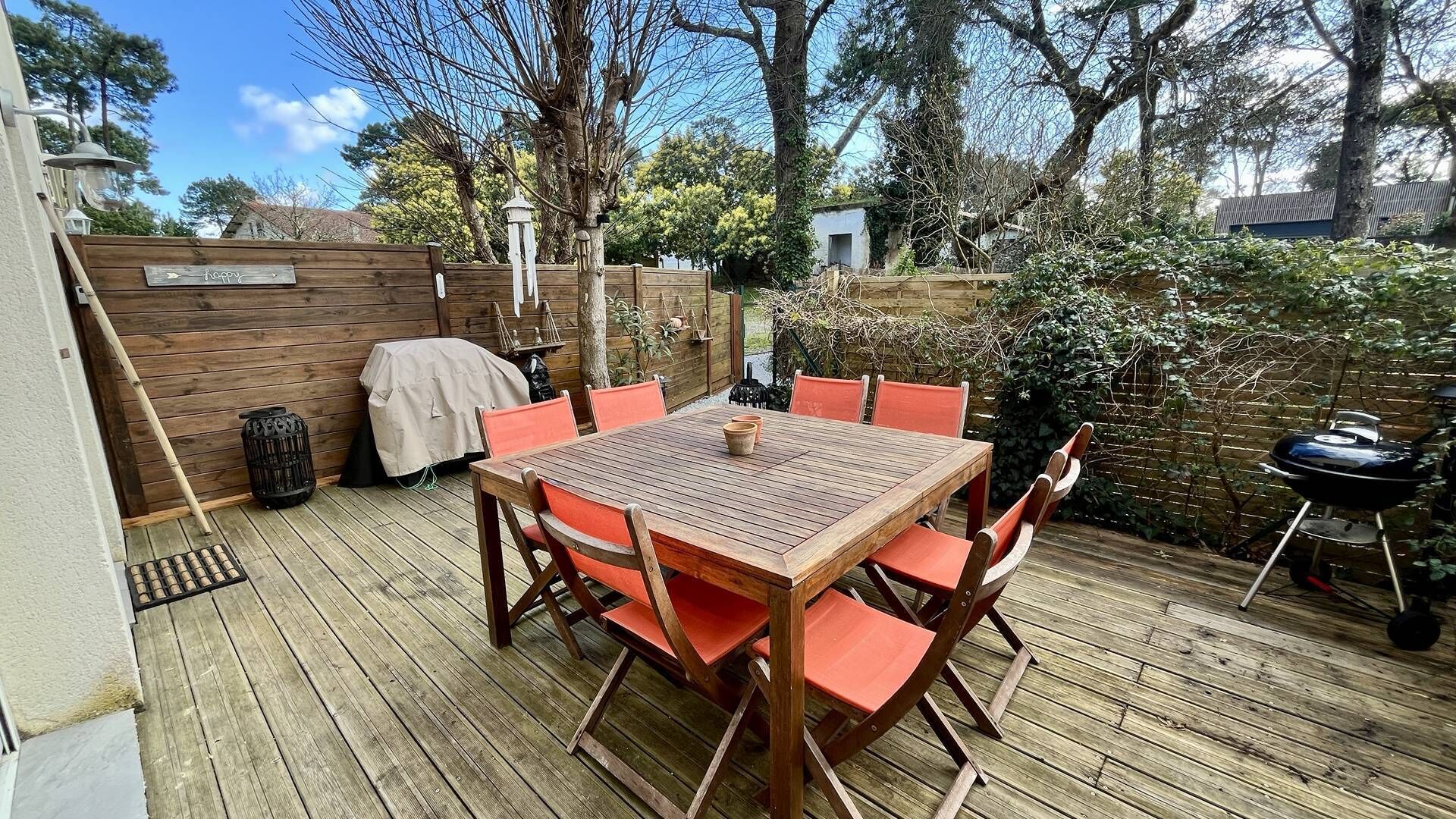 Eine Holzterrasse mit Tisch und Stühlen, einem Grill und einem überdachten Grillbereich.