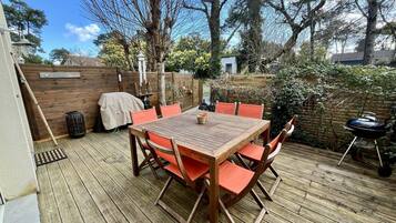 Eine Holzterrasse mit Tisch und Stühlen, einem Grill und einem überdachten Grillbereich.