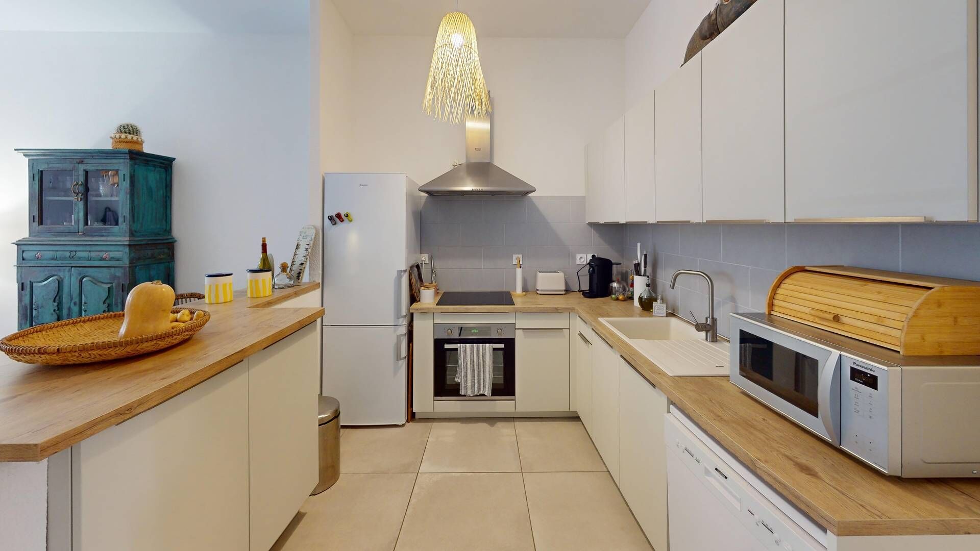 Una cocina moderna con armarios blancos, encimera de madera, horno integrado, lavavajillas y una lámpara colgante original.