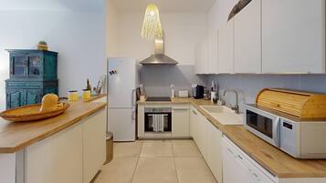Una cocina moderna con armarios blancos, encimera de madera, horno integrado, lavavajillas y una lámpara colgante original.