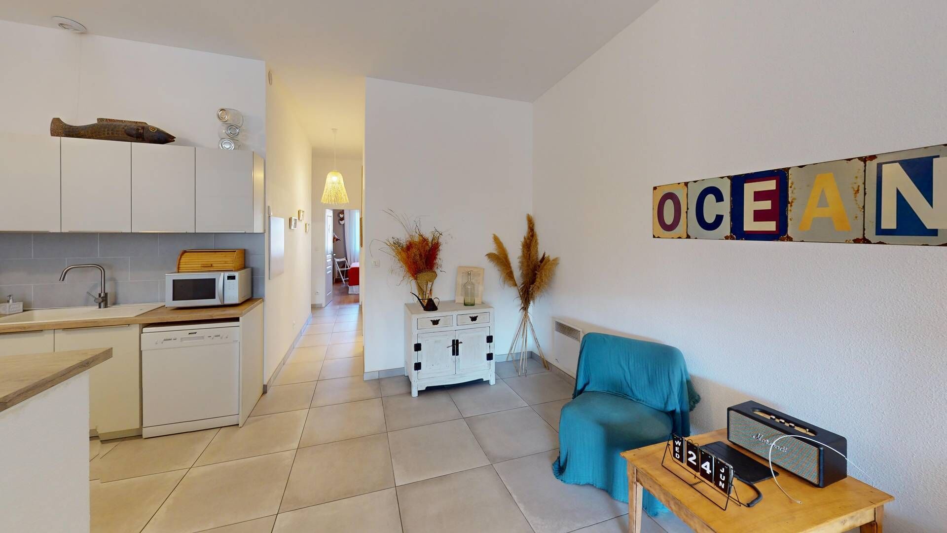 Un espacio habitable compacto con kitchenette, un sofá, una mesita de centro con radio y decorativa hierba de pampa.