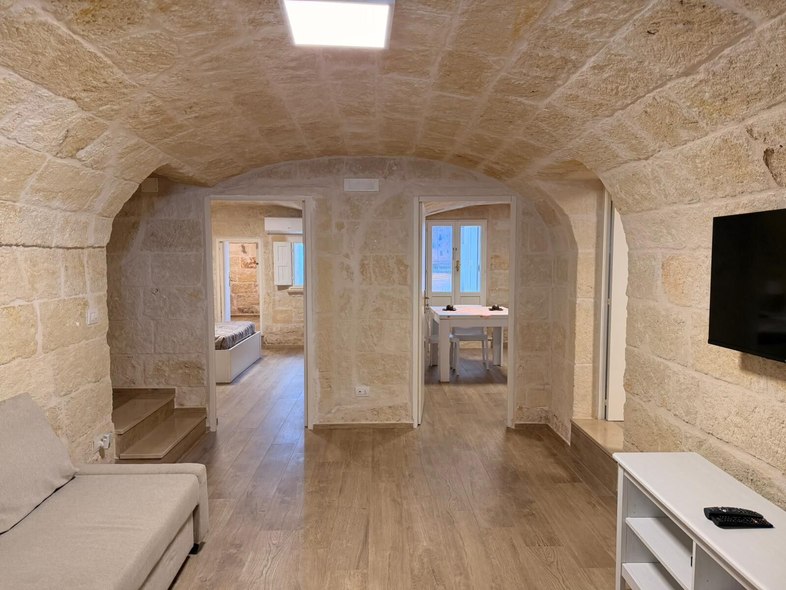 Habitación con paredes de piedra, suelo de madera, cama, televisor y zona de comedor con mesa y sillas.
