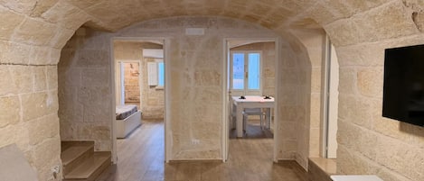 Habitación con paredes de piedra, suelo de madera, cama, televisor y zona de comedor con mesa y sillas.