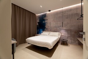 A modern bedroom with a large bed, a nightstand, a small table, and a wall with a textured design. - Solymar Mare by Monholiday (Monopoli)