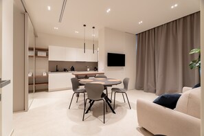 A modern living room with a sofa, a dining table with chairs, a kitchen area, and a TV mounted on the wall. - Solymar Mare by Monholiday (Monopoli)