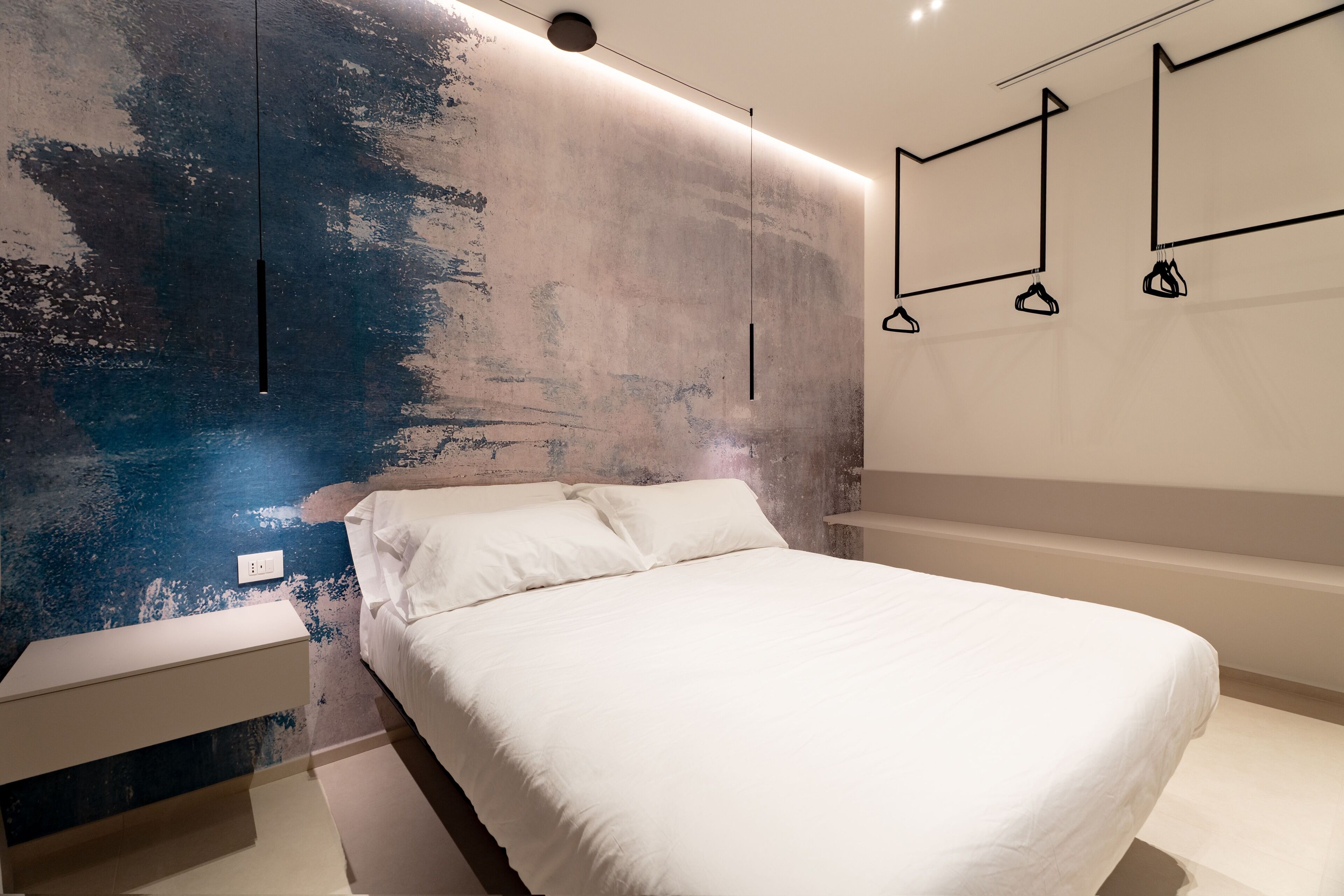 Une chambre à coucher moderne avec un lit, une table de chevet, une étagère murale et un mur à texture.