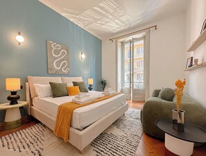 Ein Schlafzimmer mit Bett, Nachttischlampen, einem Wandbild, einem Fenster mit Blick und einem grünen Sessel.