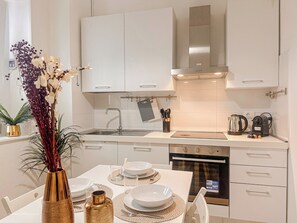 A modern kitchen with white cabinets, a stainless steel range hood, and a dining table set for four. - Flatsharing - Campanini Blue suite - 3 bedroom (Milan)