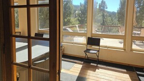 Una habitación con ventanas amplias, una terraza de madera y una silla.
