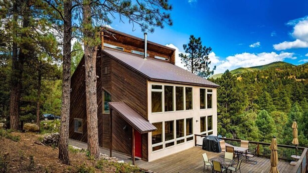 Una casa moderna con terraza, ventanas amplias y montañas al fondo.