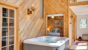 Interior de madera con una bañera de hidromasaje, una cama y una ventana.