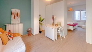 Un soggiorno moderno con un divano bianco, un'area pranzo con un tavolo bianco e una camera da letto con un letto.