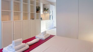 Una moderna camera d'hotel con un letto grande, un armadio a muro con diversi ripiani, angolo cottura e vista sulla città.