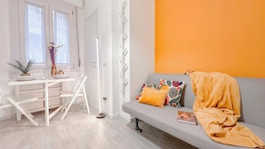 A room with a grey sofa, a small table with a plant, and a window with curtains. - Flatsharing - Campanini Orange suite (Milan)