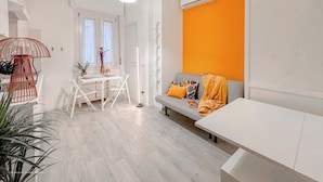 A modern living space with a dining area, a sofa with cushions, and a white table. - Flatsharing - Campanini Orange suite (Milan)