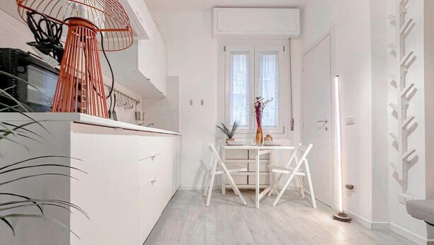 A modern kitchen with white cabinetry, a dining area with a white table and chairs, and a large window with natural light. - Flatsharing - Campanini Orange suite (Milan)