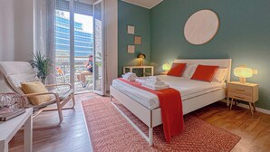 A hotel room with a bed, a chair, a bedside table, a nightstand, and a view of the outside. - Flatsharing - Gioia Blue Retreat – 3 Bedrooms (Milan)