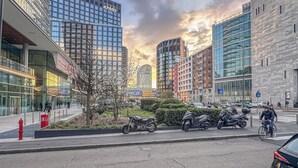 A city street with modern buildings, a clear sky, and parked motorcycles. - Flatsharing - Gioia Blue Retreat – 3 Bedrooms (Milan)