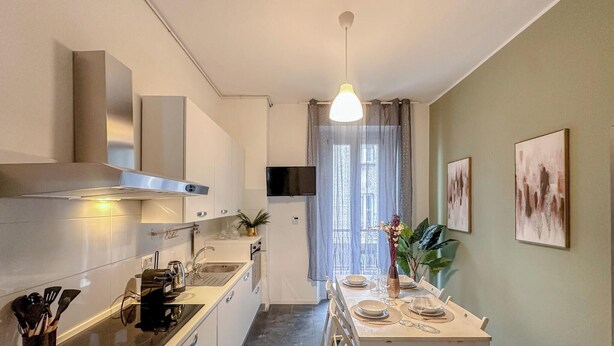 A modern kitchen with a built-in stove, a hanging light fixture, a dining area with a table set for four, and a TV mounted on the wall. - Flatsharing - Gioia Blue Retreat – 3 Bedrooms (Milan)