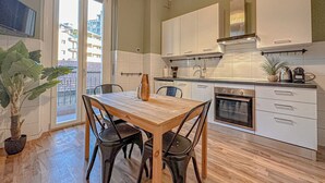 Une cuisine moderne avec un coin repas, comprenant une table et des chaises en bois, un four encastré et une vue à travers une porte vitrée.