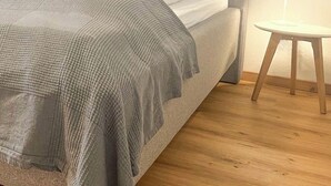 A bed with a grey headboard, white bedding, and a grey throw blanket. There is a small round table with a lamp beside the bed. - Renovated, beautifully furnished vacation home "Sannchen" with great attention to detail (Dahlem)