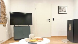 A modern living room with a flat-screen TV, a small round table with a woven placemat, a remote control, and a decorative glass vase. - Renovated, beautifully furnished vacation home "Sannchen" with great attention to detail (Dahlem)