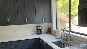 A modern kitchen with dark cabinets, a white countertop, a built-in dishwasher, and a window with a view of the outdoors. - Modern Manchester Condo (Manchester)