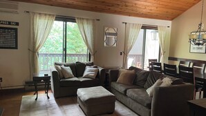 A cozy living room with a wooden ceiling, two couches, a small table, and a dining area with chairs. - Modern Manchester Condo (Manchester)