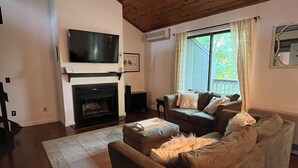 A living room with a fireplace, a sofa, a television, and a window with curtains. - Modern Manchester Condo (Manchester)