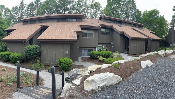 A modern multi-story building with a curved roof, a gravel driveway, and landscaped gardens. - Modern Manchester Condo (Manchester)