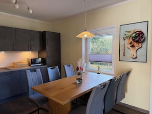 Een moderne keuken met donkere kastjes, een houten eettafel en een raam met uitzicht op groen.
