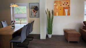 Ein Essbereich mit Holztisch, Stühlen, einer Pendelleuchte, einer Topfpflanze und Kunstwerken an der Wand.