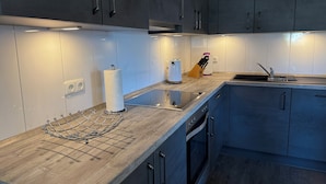 Eine moderne Küche mit dunklen Schränken, einer Holzarbeitsplatte, einem Wasserkocher, einem Messerblock und einem eingebauten Backofen.
