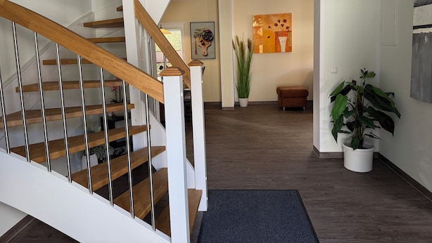 Eine Treppe mit Holzstufen und weißen Geländern, die zu einem Raum führt, in dem eine große Pflanze und Kunstwerke an der Wand zu sehen sind.