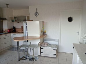 Eine kompakte Küche mit Kühlschrank, Mikrowelle, Kaffeemaschine und einer kleinen Essecke mit zwei Stühlen.