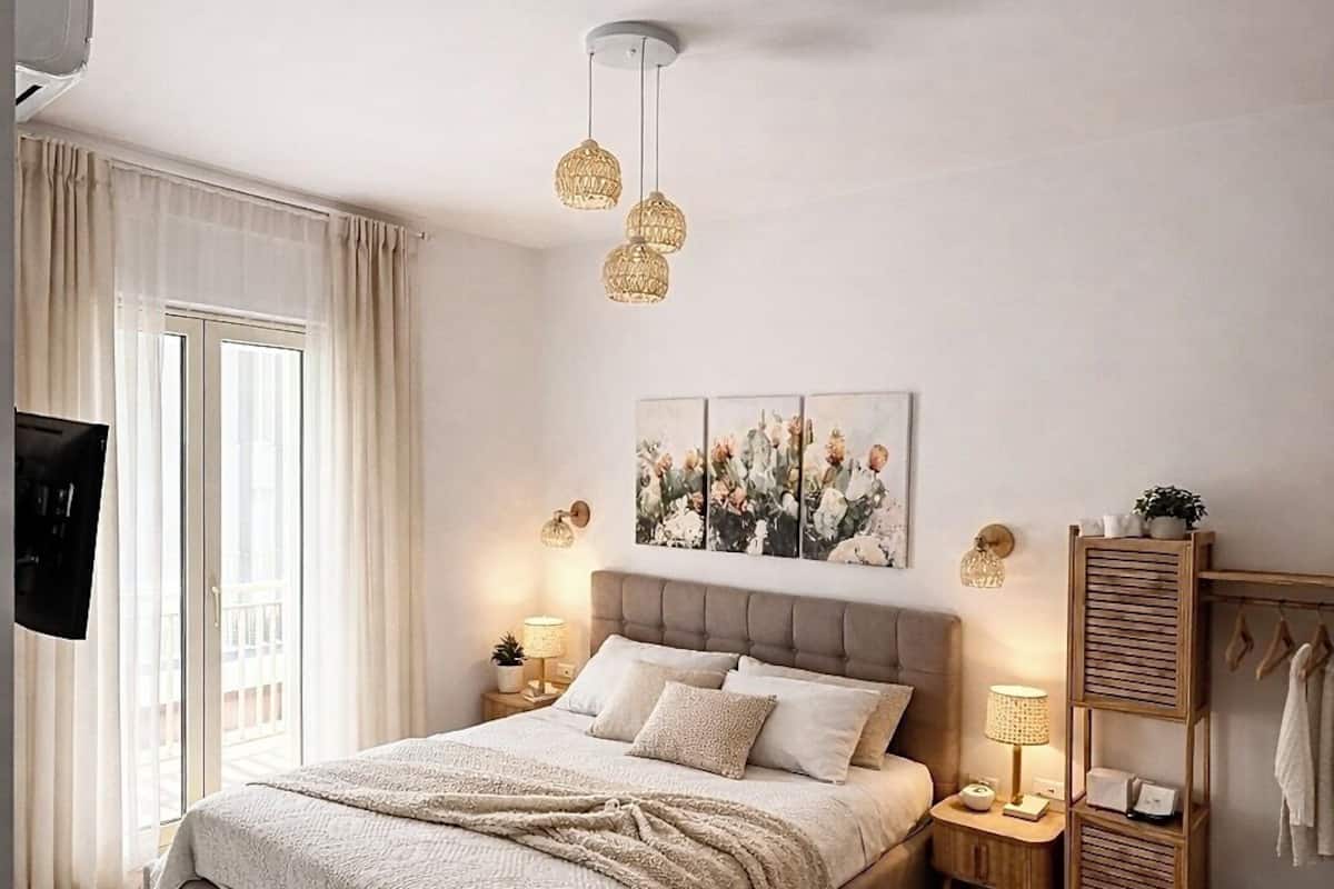 A bedroom with a bed, bedside tables, a TV, a painting, and a wooden rack with towels.